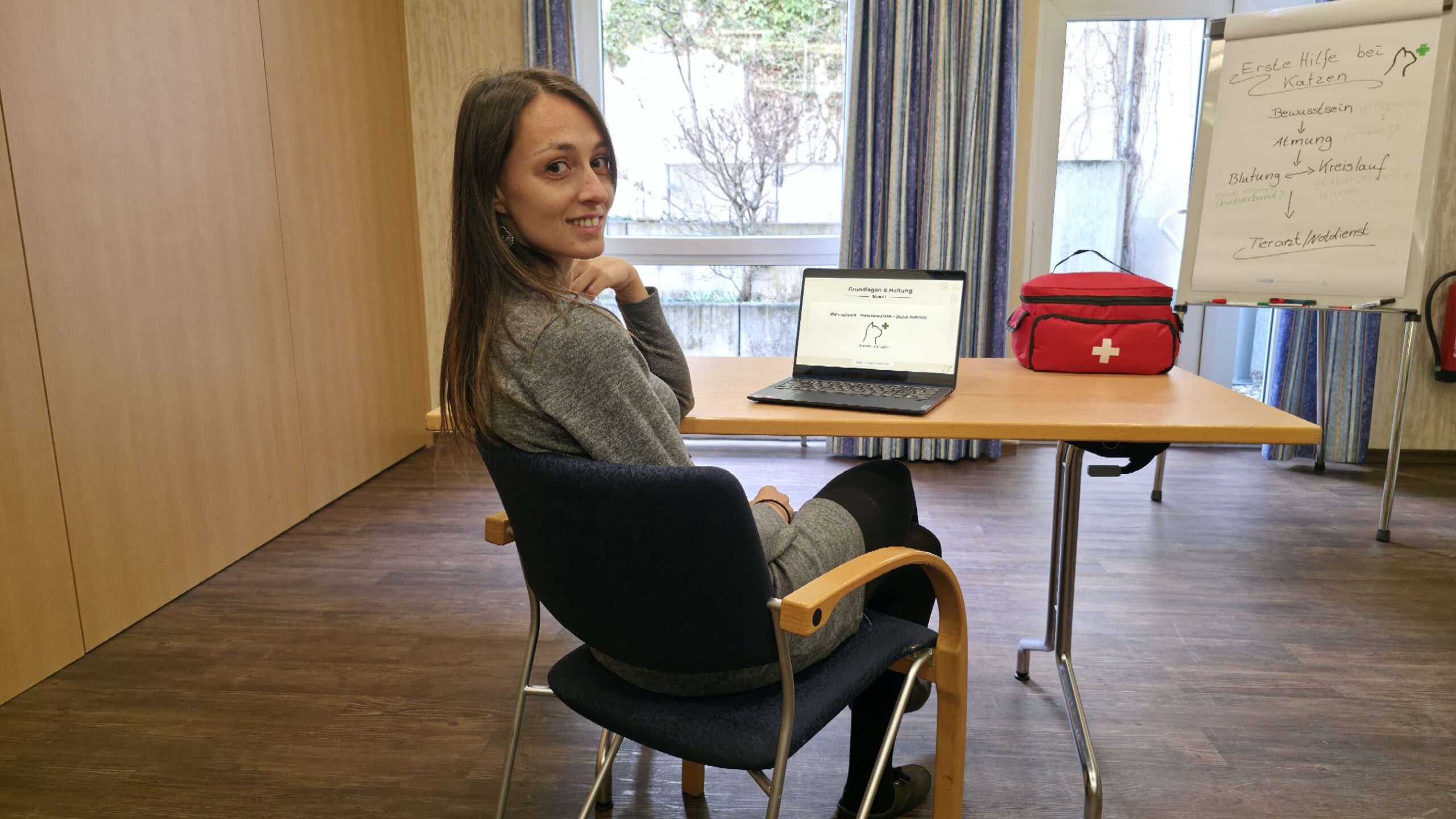 Sarah, Erste-Hilfe-Ausbilderin, am Tisch mit Laptop und Erste-Hilfe-Tasche